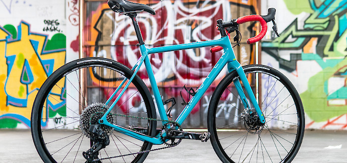 A custom-built blue Open Cycles Wi.De gravel bike against a colourful graffitied wall