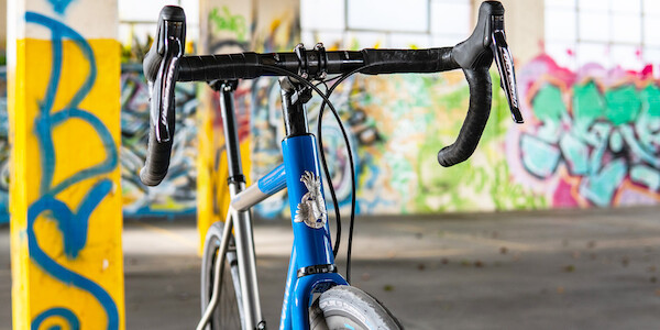 Curve Belgie titanium bike with a custom paint job, viewed from a three-quarter angle, in front of a colourful graffitied wall