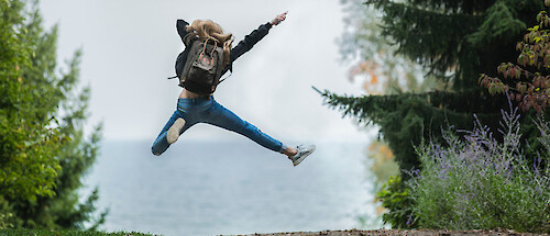 A woman in a forest setting, leaping for joy, viewed from behind.