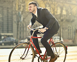 A man riding a red bicycle in a city street, grimacing and looking uncomfortable