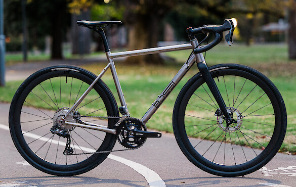 A Bossi Grit SX titanium gravel bike in a custom build, freestanding on a city cycle path. How does it stay up? It's a mystery!