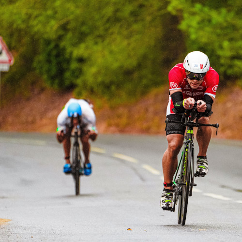 Front view of two road cyclists racing down a hill, one using the time-trial bars on his bike