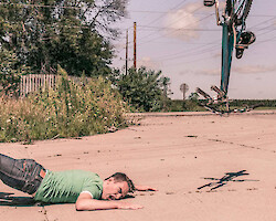 A man crashing to the ground during a bike accident, his bicycle flying off in pieces