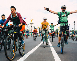 A bunch of people riding bikes along the road towards the camera. One man has his arms spread out in an expression of joy.