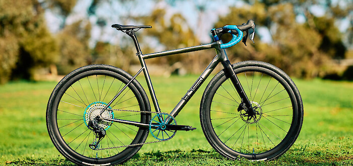 A custom-built Bossi Grit SS titanium gravel bike in a green field